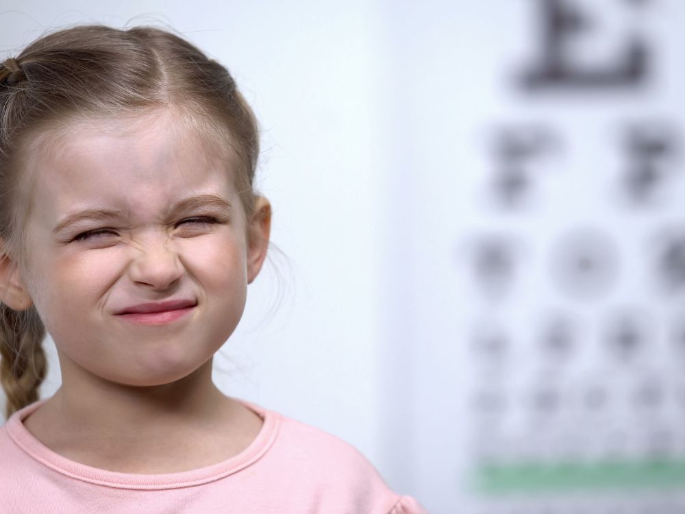 Criança forçando os olhos para enxergar melhor, comportamento comum em casos de o que é visão distorcida e outras alterações na visão infantil.