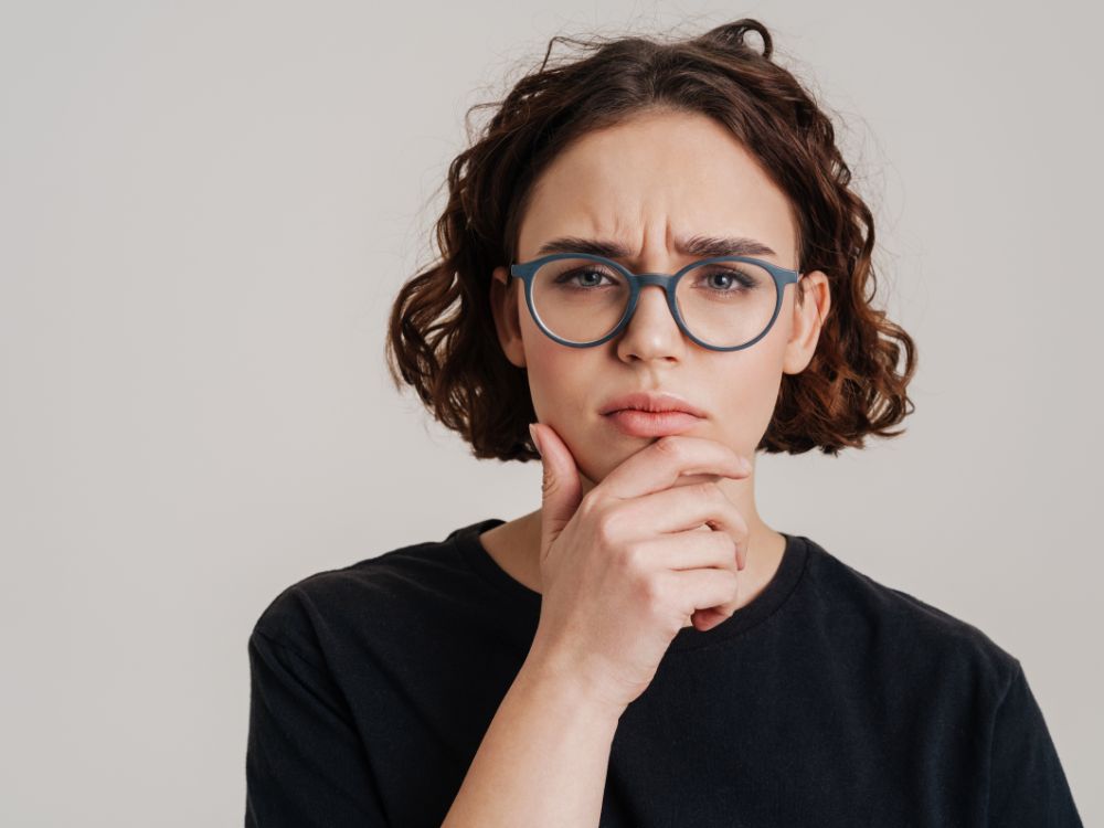 Mulher de óculos com expressão pensativa, representando a incerteza sobre se óculos de descanso precisa de exame.
