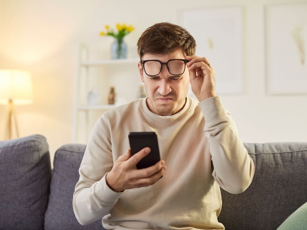 Homem com miopia forçando a visão para ler no celular, exemplo comum entre pessoas que buscam entender como diminuir o grau de miopia.