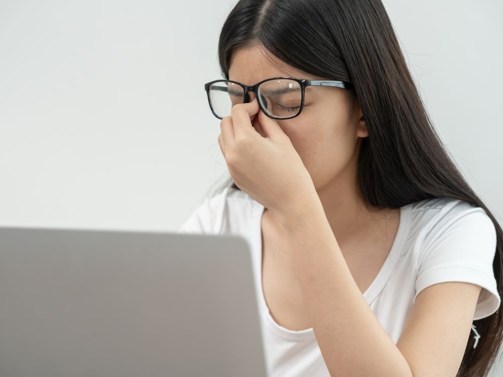 Mulher com óculos sentindo fadiga ocular em frente ao computador, ilustrando a importância de cuidados diários sobre como diminuir o grau de miopia.