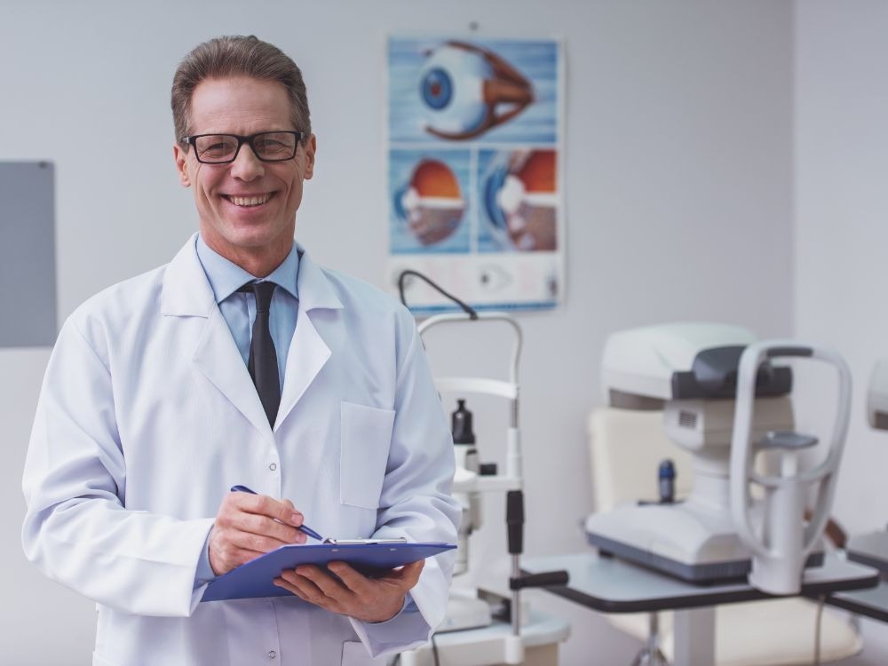Oftalmologista sorridente em consultório equipado com aparelhos de exame, indicando atendimento especializado para A DMRI seca.