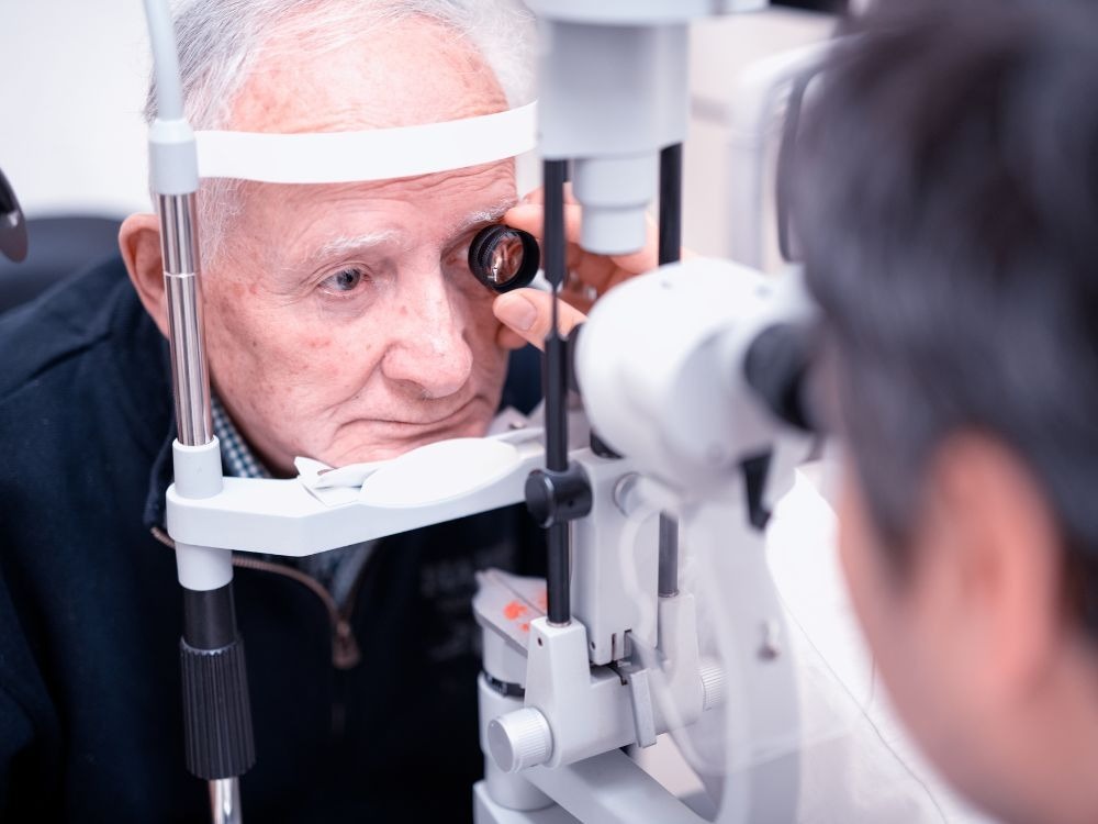 Paciente idoso realizando exame de fundo de olho no equipamento oftalmológico, parte do diagnóstico de A DMRI seca.