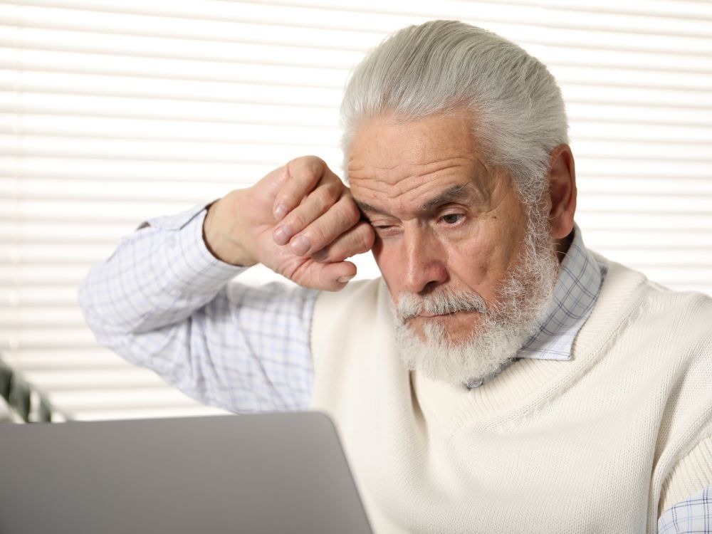 Idoso sentado diante do computador esfregando os olhos por desconforto visual, representando sinais comuns de A DMRI seca.
