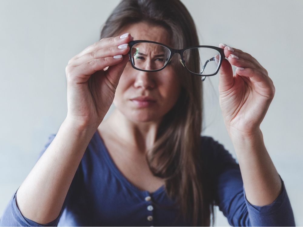Mulher observa óculos com dificuldade de foco, representando a preocupação de quem convive com problemas visuais e questiona se miopia pode cegar.