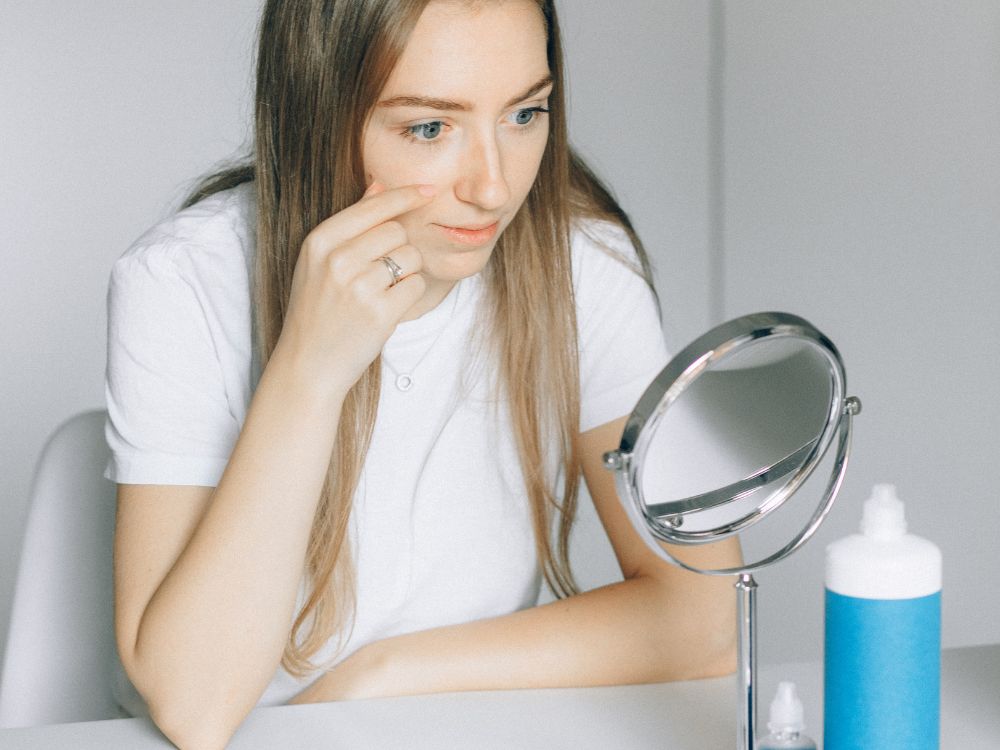 Mulher observando os olhos no espelho enquanto avalia possíveis Sintomas na adaptação de lentes de contato durante os primeiros dias de uso.