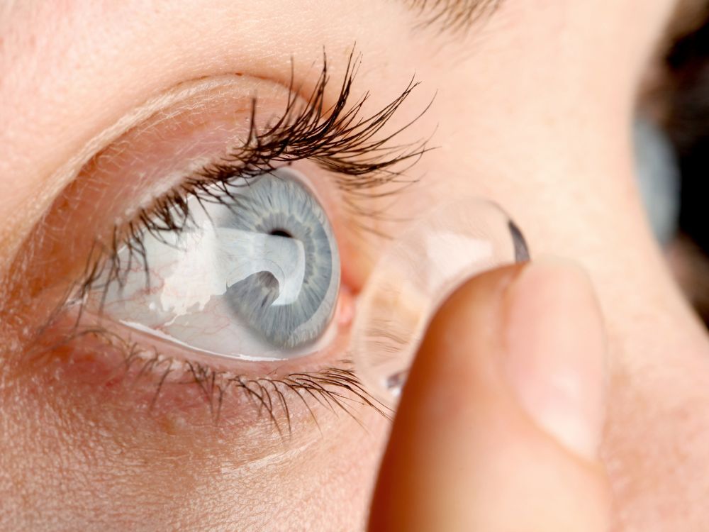 Close no olho de pessoa colocando lente de contato, ilustrando Sintomas na adaptação de lentes de contato como sensibilidade e lacrimejamento.